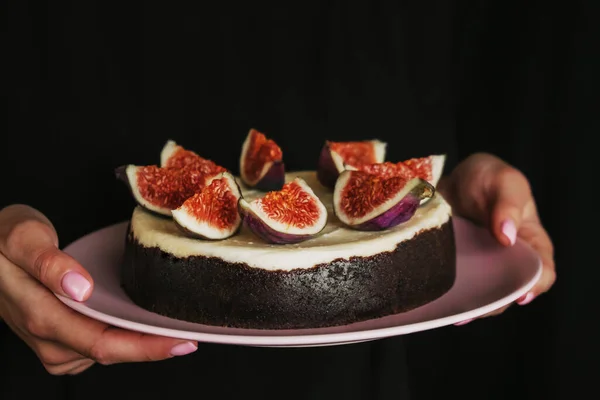 Женщина, держащая розовую тарелку с чизкейком. шоколадный десерт со свежим инжиром на темном черном фоне. минимализм дизайн торта. женская рука с розовыми ногтями, свежий маникюр — стоковое фото