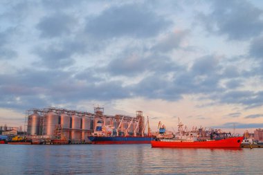 Nakliye gemisi nehir limanında. Kuru kargo tahıl asansörü ticareti. Tarım Denizi Tesisi. Kargo gemisi. Gün batımı manzarası. Sudaki fabrika.