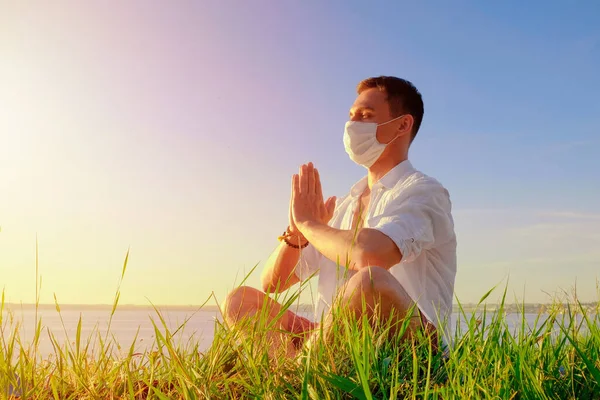 Hombre haciendo yoga sentado en una pose de loto usando mascarilla de PPE. entrenamiento al aire libre después de la cuarentena. hacer frente al pánico, la ansiedad, la pandemia mundial. medidas de seguridad covid-19. nuevas regulaciones de crisis realidad . — Foto de Stock