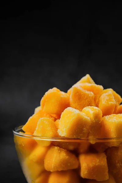 frozen mango cubes covered in thin ice in a glass ball with hoarfrost on black background. preserved vitamins. frozen fruit product. winter food preservation. cold meal from the freezer. fast freeze