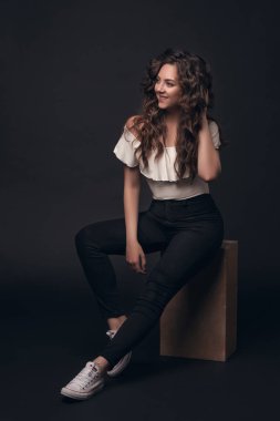 Şık giysiler içinde uzun kıvırcık saçlı genç şık kız modeli metin için yer karanlık bir yalıtılmış zemin üzerine oturur