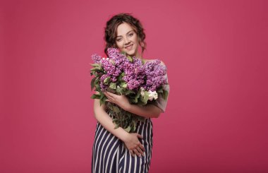 Şık giysiler içindeki genç bir ince kız mor çiçekler Buket tutuyor. O, o bir tarihte verildi hediye şaşırır. Pembe bir arka plan üzerinde metin için yer ile