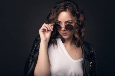 Bir deri ceket, karanlık bir arka plan üzerinde şık bir saç modeli ile genç bir esmer kız beyaz tişört ve güneş gözlüğü. Profesyonel model izole koyu arka plan metin için yer ile poz