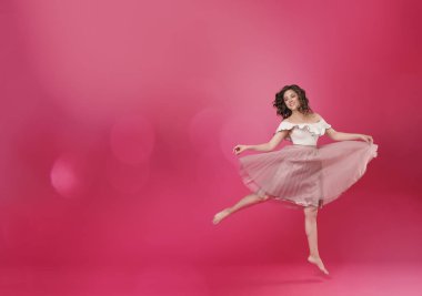 Şık kız pembe ışık etek ve metin için yer pembe yalıtılmış zemin üzerine beyaz T-shirt. Kız neşeyle dans ediyor ve bir balerin gibi atlar