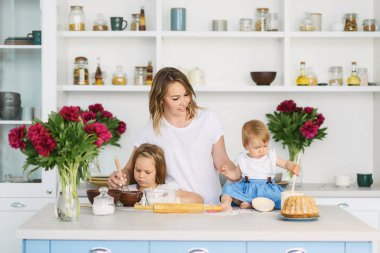 Onun iki çocuklu genç bir anne büyük ve parlak mutfakta lezzetli ve sağlıklı yemek hazırlanıyor. kadın öğretir çocuklar nasıl hamur yapmak