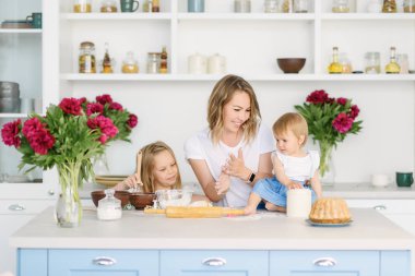 Onun iki çocuklu genç bir anne büyük ve parlak mutfakta lezzetli ve sağlıklı yemek hazırlanıyor. kadın öğretir çocuklar nasıl hamur yapmak