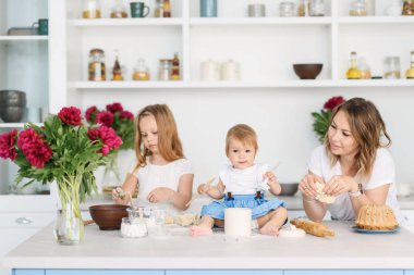Onun iki çocuklu genç bir anne büyük ve parlak mutfakta lezzetli ve sağlıklı yemek hazırlanıyor. kadın öğretir çocuklar nasıl hamur yapmak