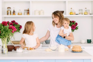 Onun iki çocuklu genç bir anne büyük ve parlak mutfakta lezzetli ve sağlıklı yemek hazırlanıyor. kadın öğretir çocuklar nasıl hamur yapmak
