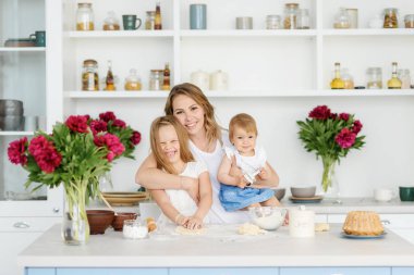 Onun iki çocuklu genç bir anne büyük ve parlak mutfakta lezzetli ve sağlıklı yemek hazırlanıyor. kadın öğretir çocuklar nasıl hamur yapmak