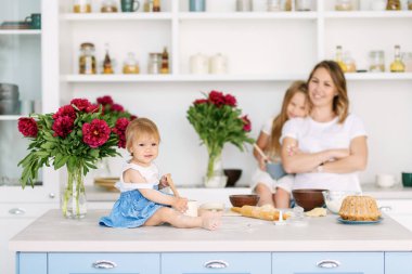 Onun iki çocuklu genç bir anne büyük ve parlak mutfakta lezzetli ve sağlıklı yemek hazırlanıyor. kadın öğretir çocuklar nasıl hamur yapmak