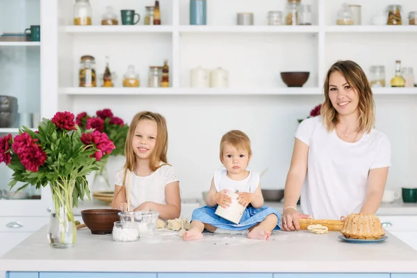 Onun iki çocuklu genç bir anne büyük ve parlak mutfakta lezzetli ve sağlıklı yemek hazırlanıyor. kadın öğretir çocuklar nasıl hamur yapmak