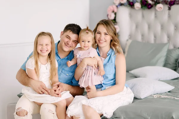 Aile portresi. Anne Anne ve baba ile iki güzel kızı büyük bir parlak odada yatakta oturuyor. Ebeveynler çocuklarını sarılmak ve onlar mutlular