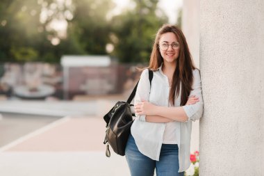 Gözlüklü bir öğrenci kız portresi. Parkın arka planda duruyor ve Notebook ve klasörleri onun elinde tutar. Kız üniversiteye girmek hazırlanıyor