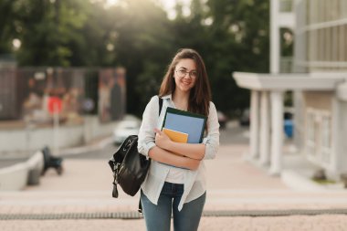Gözlüklü bir öğrenci kız portresi. Parkın arka planda duruyor ve Notebook ve klasörleri onun elinde tutar. Kız üniversiteye girmek hazırlanıyor