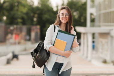 Gözlüklü bir öğrenci kız portresi. Parkın arka planda duruyor ve Notebook ve klasörleri onun elinde tutar. Kız üniversiteye girmek hazırlanıyor