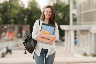 Gözlüklü bir öğrenci kız portresi. Parkın arka planda duruyor ve Notebook ve klasörleri onun elinde tutar. Kız üniversiteye girmek hazırlanıyor