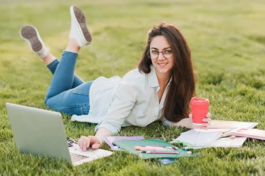 Genç bir öğrenci üniversitenin önünde yeşil çim üzerinde yatıyor ve final sınavları için hazırlanıyor. O bilimsel makaleler internette tarar ve yararlı notlar not defterinde yapar