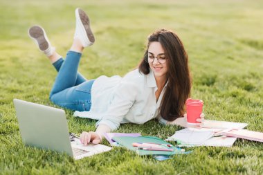 Genç bir öğrenci üniversitenin önünde yeşil çim üzerinde yatıyor ve final sınavları için hazırlanıyor. O bilimsel makaleler internette tarar ve yararlı notlar not defterinde yapar