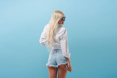 Uzun saçlı Genç ince sarışın kız ile mavi bir arka plan sırtında duruyor ve onun kulaklıktan müzik parçaları. Model kısa şort ve güneş gözlüğü dans ediyor sevinçle