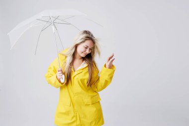 Yağmur yağıyor, hava kontrol şeffaf şemsiye tutan sarı yağmurluk giymiş sarışın kadın. Yağmur ve fırtına karşı korumalı