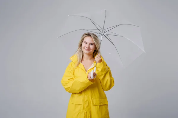 Blond kvinna klädd i gul regnrock innehar transparent paraply kontrollera vädret om det regnar. Skyddad mot regn- och orkansäsongen — Stockfoto