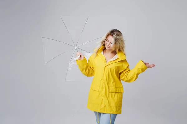 Szőke nő visel a sárga esőkabátot gazdaság átlátszó esernyő, időjárás ellenőrzése, ha esik az eső. Eső és hurrikán ellen védett — Stock Fotó