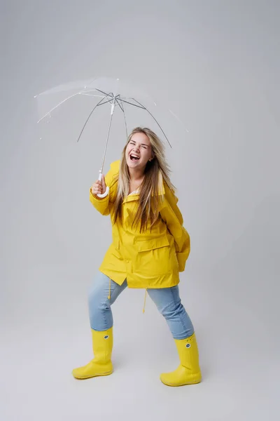 Blonde woman wearing yellow raincoat holding transparent umbrella checking weather if it is raining. Protected against rain and hurricane