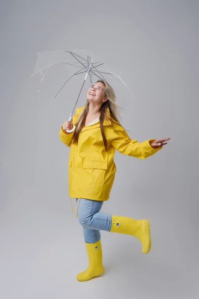 Blonde woman wearing yellow raincoat holding transparent umbrella checking weather if it is raining. Protected against rain and hurricane