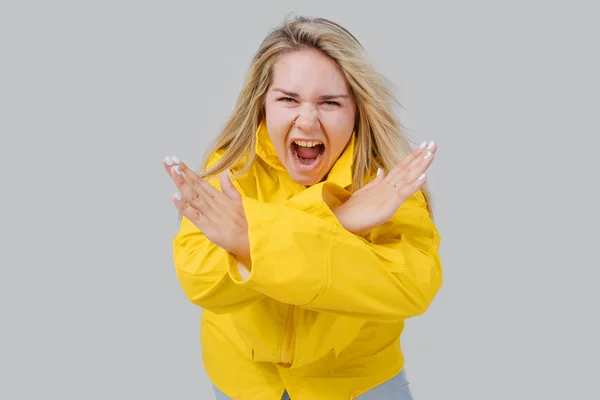 Ξανθιά νεαρή γυναίκα σε ένα κίτρινο αδιάβροχο φοβάται της βροχής. Προσπαθεί να σταματήσει τα χέρια ενός τυφώνα — Φωτογραφία Αρχείου