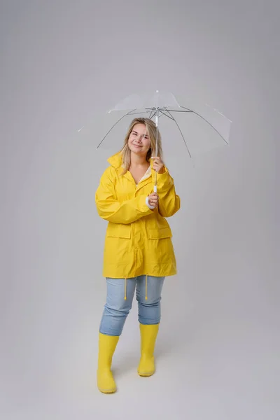 Mulher loira usando capa de chuva amarela segurando guarda-chuva transparente verificando o tempo se estiver chovendo. Protegido contra chuva e furacão — Fotografia de Stock