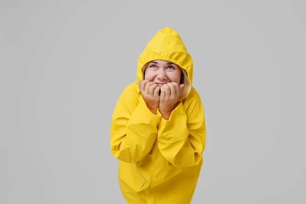 Blondýnka mladá žena v žlutá pláštěnka s kapucí na hlavě pozadí skrývá před deštěm na šedém pozadí — Stock fotografie
