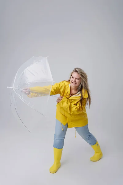 Blonde vrouw draagt gele regenjas holding transparante paraplu controleren weer als het regent. Beschermd tegen regen en orkaan — Stockfoto