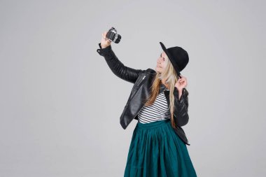 Moda, güzel genç kadın modeli retro film kamera ile görünmesi selfie. bir şık şapka, siyah ceket, blondy saç açık havada gri arka plan üzerinde giyen