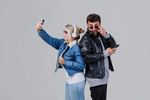 Portrait of a young couple enjoying music and make selfie over grey background
