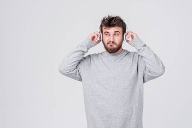 Genç bir adam rahat kıyafetler içinde sakallı kablosuz kulaklık hoş müzik dinler. Metin için yer ile gri arka plan