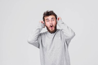 Şok. Yüzünde korku ile rahat kıyafetler içinde sakallı genç bir adam kablosuz kulaklık yüksek sesle müzik dinler. Metin için yer ile gri arka plan