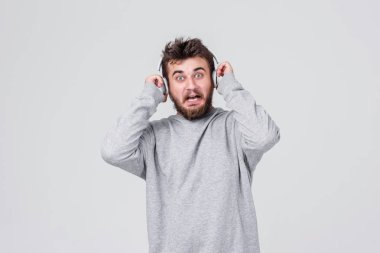 Şok. Yüzünde korku ile rahat kıyafetler içinde sakallı genç bir adam kablosuz kulaklık yüksek sesle müzik dinler. Metin için yer ile gri arka plan