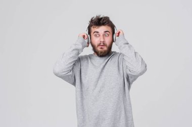 Şok. Yüzünde korku ile rahat kıyafetler içinde sakallı genç bir adam kablosuz kulaklık yüksek sesle müzik dinler. Metin için yer ile gri arka plan