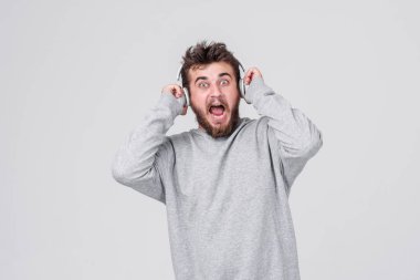 Şok. Yüzünde korku ile rahat kıyafetler içinde sakallı genç bir adam kablosuz kulaklık yüksek sesle müzik dinler. Metin için yer ile gri arka plan
