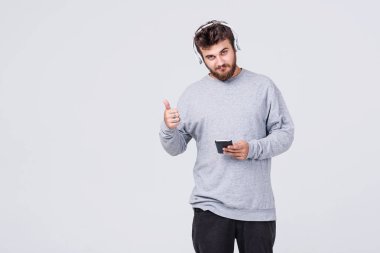 Günlük giysiler içinde sakallı genç bir adam onun cep telefonu kablosuz kulaklık aracılığıyla radyo dinlediğini. O jestleri ile onun Tamam parmak. Metin için yer ile gri arka plan