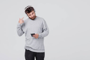 Rahat kıyafetler içinde sakallı genç bir adam onun cep telefonu kablosuz kulaklık aracılığıyla radyo dinlediğini. Parmağını kulağına koyar. Metin için yer ile gri arka plan