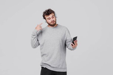 Rahat kıyafetler içinde sakallı genç bir adam onun cep telefonu kablosuz kulaklık aracılığıyla radyo dinlediğini. Parmağını kulağına koyar. Metin için yer ile gri arka plan