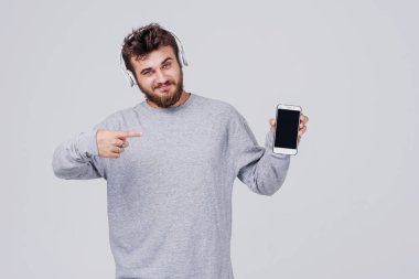 Rahat kıyafetler içinde sakallı genç bir adam onun cep telefonu kablosuz kulaklık aracılığıyla radyo dinlediğini. Belgili tanımlık becerikli alet parmağını gösteriyor. Metin için yer ile gri arka plan