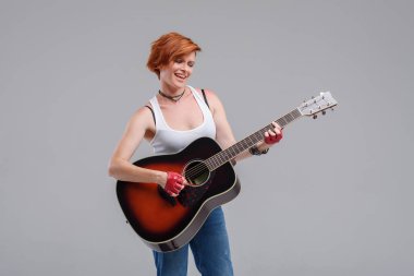 Gri bir arka plan üzerinde elinde bir akustik gitar ile genç kadın müzisyen. O gülüyor ve rock'n roll yüksek sesle çalar. 
