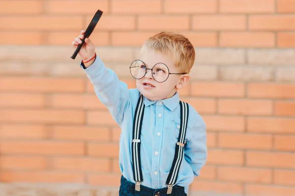 学校に戻るグラスのバックパックで幸せな男の子と 学校の建物のレンガの壁に虫眼鏡 — ストック写真