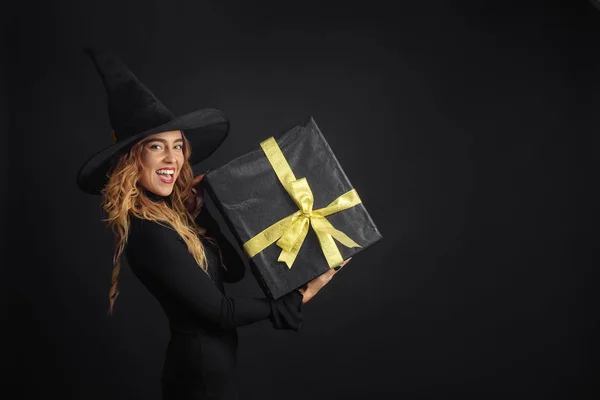 黑色星期五 万圣节女巫与黑色的帽子在黑色背景拿着礼物盒与朱斯在她的手中 惊喜和礼品在售 — 图库照片