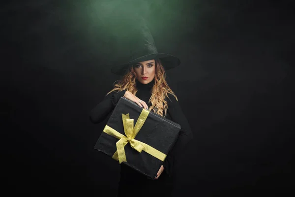 ブラックフラ イデー 彼女の手で Juruse とギフト ボックスを保持する黒い背景に黒い帽子のハロウィーンの魔女 ギフト販売 — ストック写真