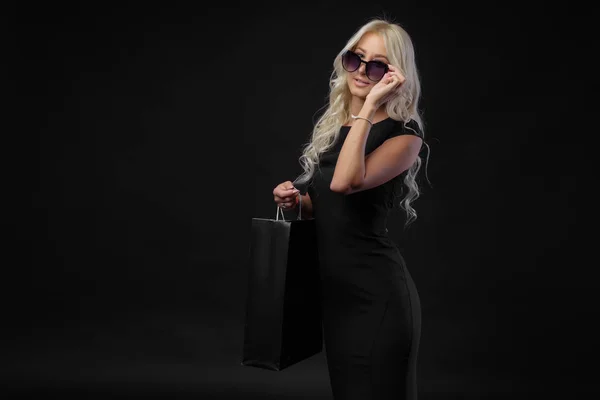 Elegante Mujer Rubia Lleva Gafas Sol Vestido Negro Sosteniendo Bolsas — Foto de Stock