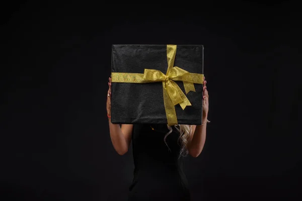 Young woman in black holding stack of gift boxes with gold ribbon. Black Friday concept