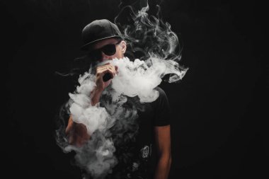Vape adam. Bir modern siyah kap vaping ve Elektronik Sigara Buhar puffs kapalı icar yakışıklı genç bir beyaz adam portresi